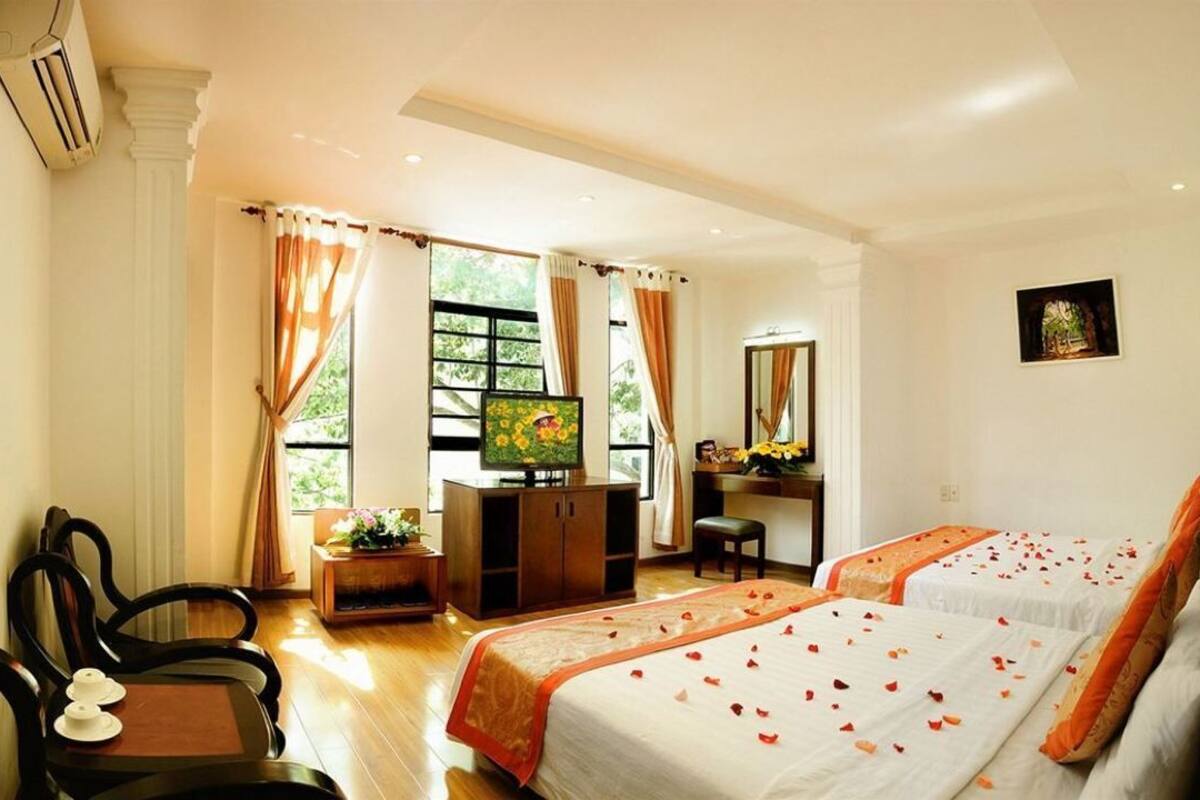 Une chambre d’hôtel avec deux lits, un bureau, une chaise et une grande fenêtre.