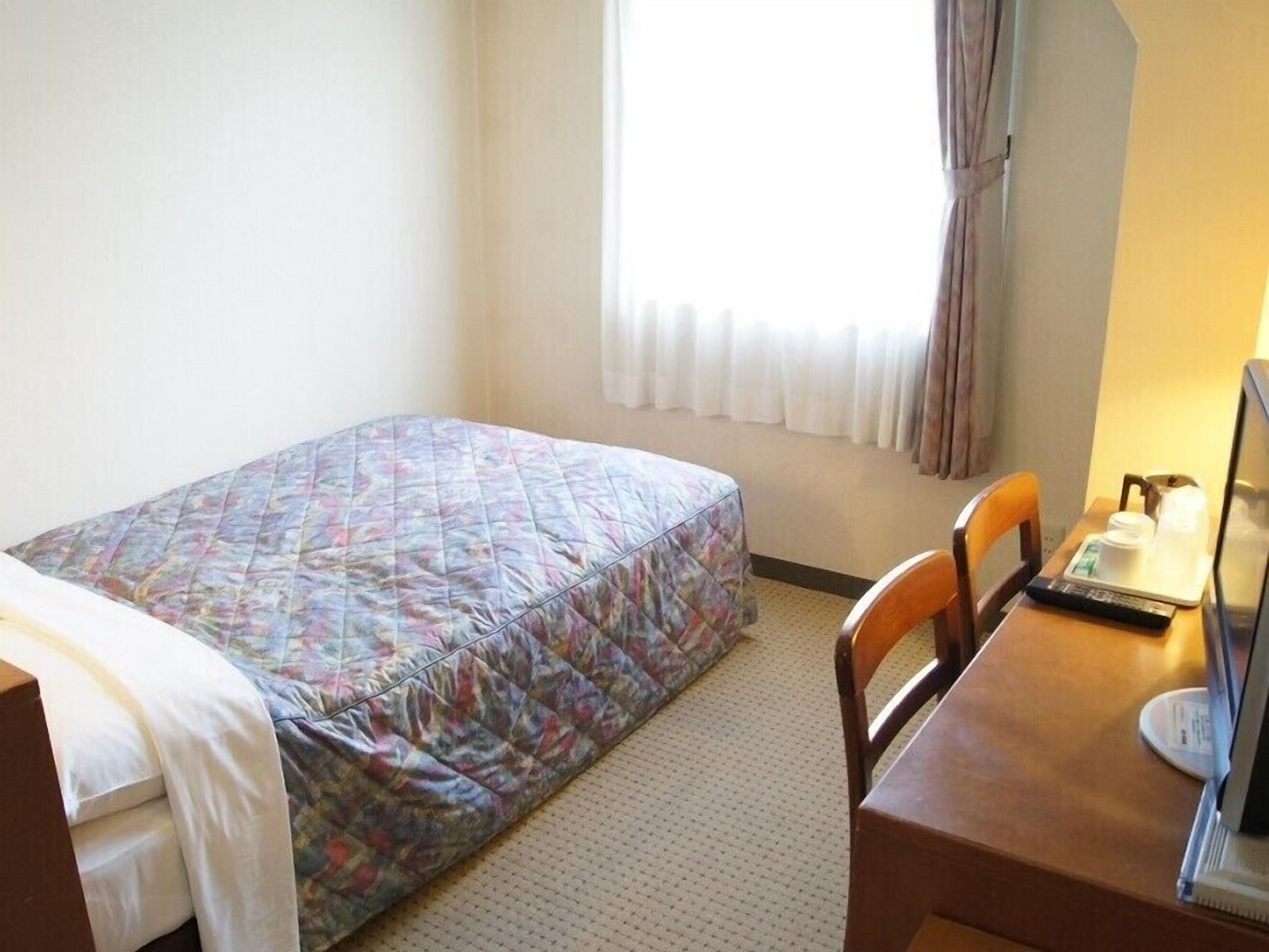 A hotel room with a bed, a desk with a computer, and a window with curtains.