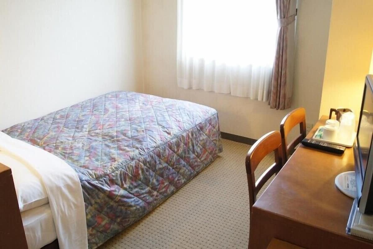 Quarto de hotel com cama, escrivaninha com computador e janela com cortinas.