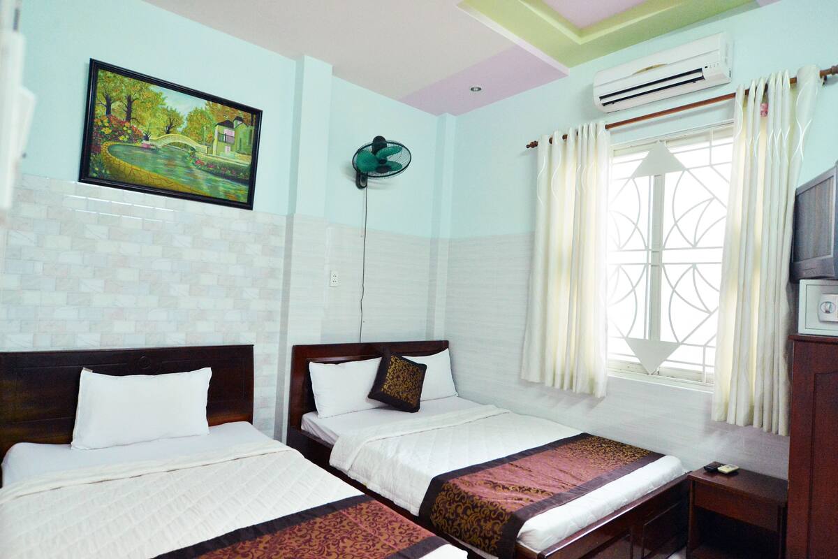 Habitación de hotel con dos camas, un cuadro en la pared, aire acondicionado y una ventana con cortinas.