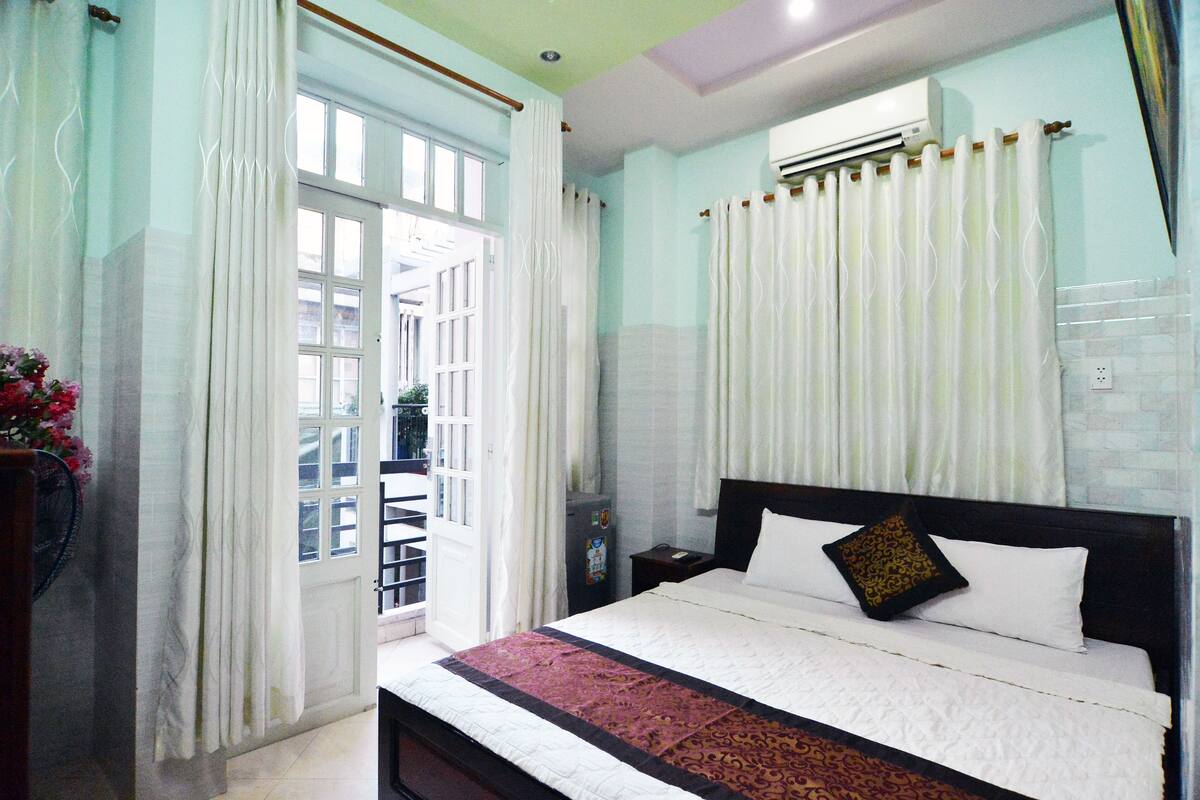 Una habitación de hotel con cama, mesita de noche, aire acondicionado y ventana con cortinas.