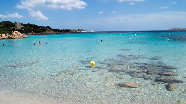 A clear beach with visible rocks and a yellow ball in the water.