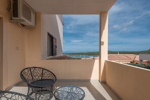 Een balkon met twee stoelen en uitzicht op zee, met een gebouw met een rood dak.