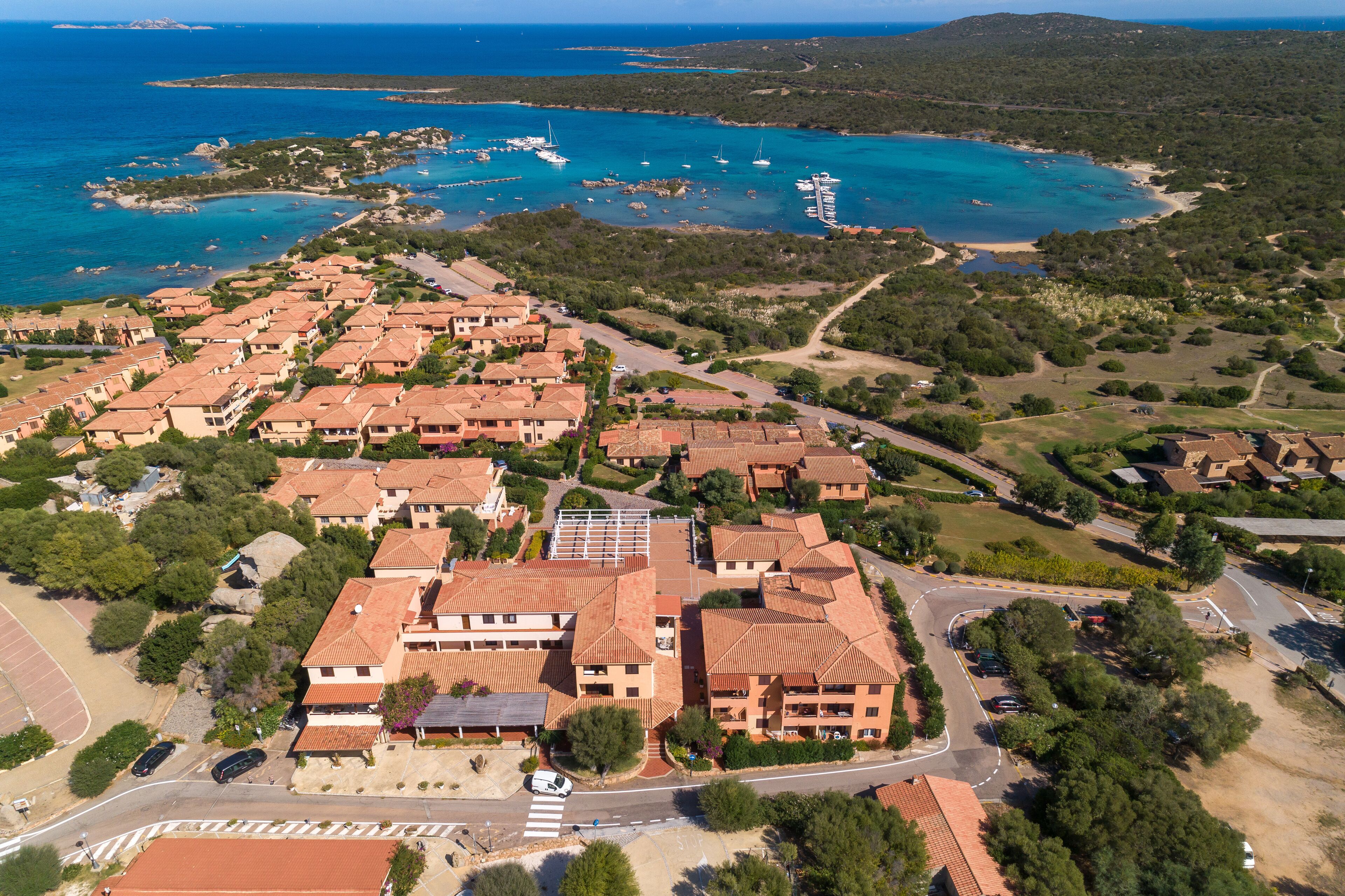 A coastal residential area with terracotta-roofed buildings, a marina, and a beach.