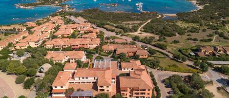A coastal residential area with terracotta-roofed buildings, a marina, and a beach.