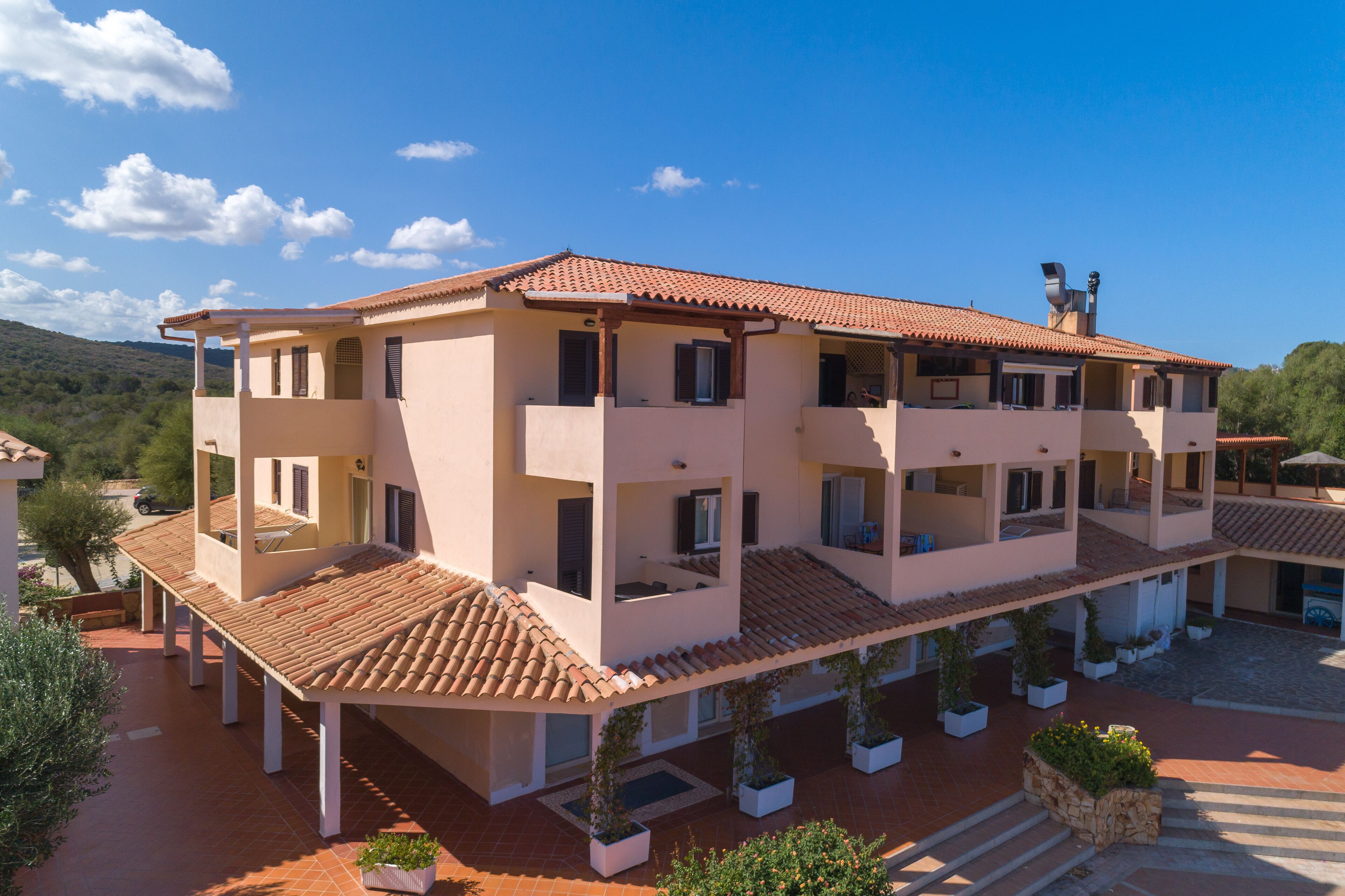 Un edificio a più piani con tetto in tegole, balconi e un cortile con piante in vaso.