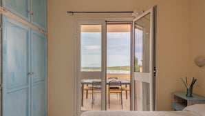 A bedroom with a bed, a wardrobe, a balcony with a table and chairs, and a view of the sea.