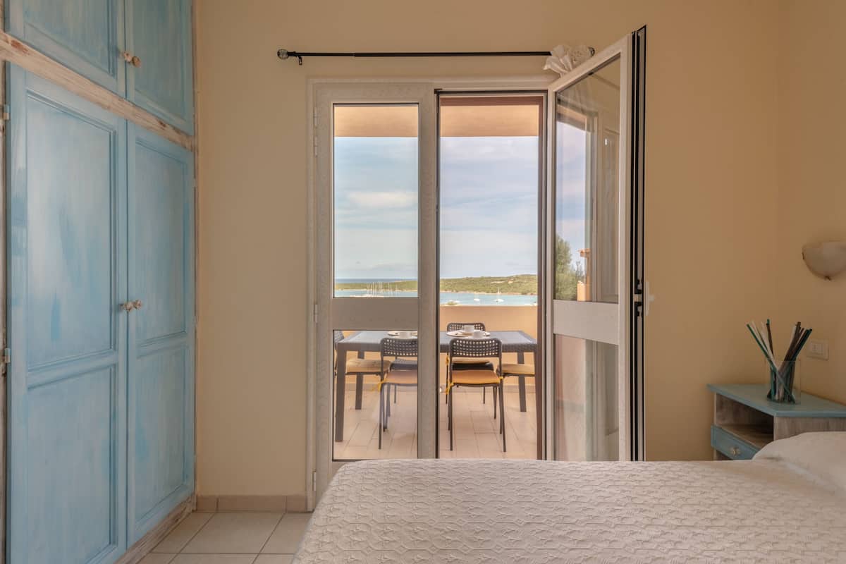 Une chambre avec un lit, une armoire, un balcon avec une table et des chaises, et une vue sur la mer.