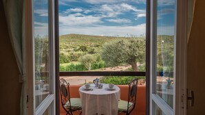 A balcony with a table set for two, overlooking a hilly landscape with trees and a clear sky.