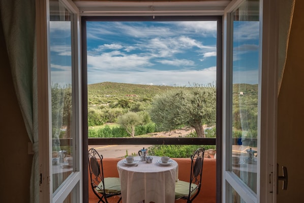 A balcony with a table set for two, overlooking a hilly landscape with trees and a clear sky.