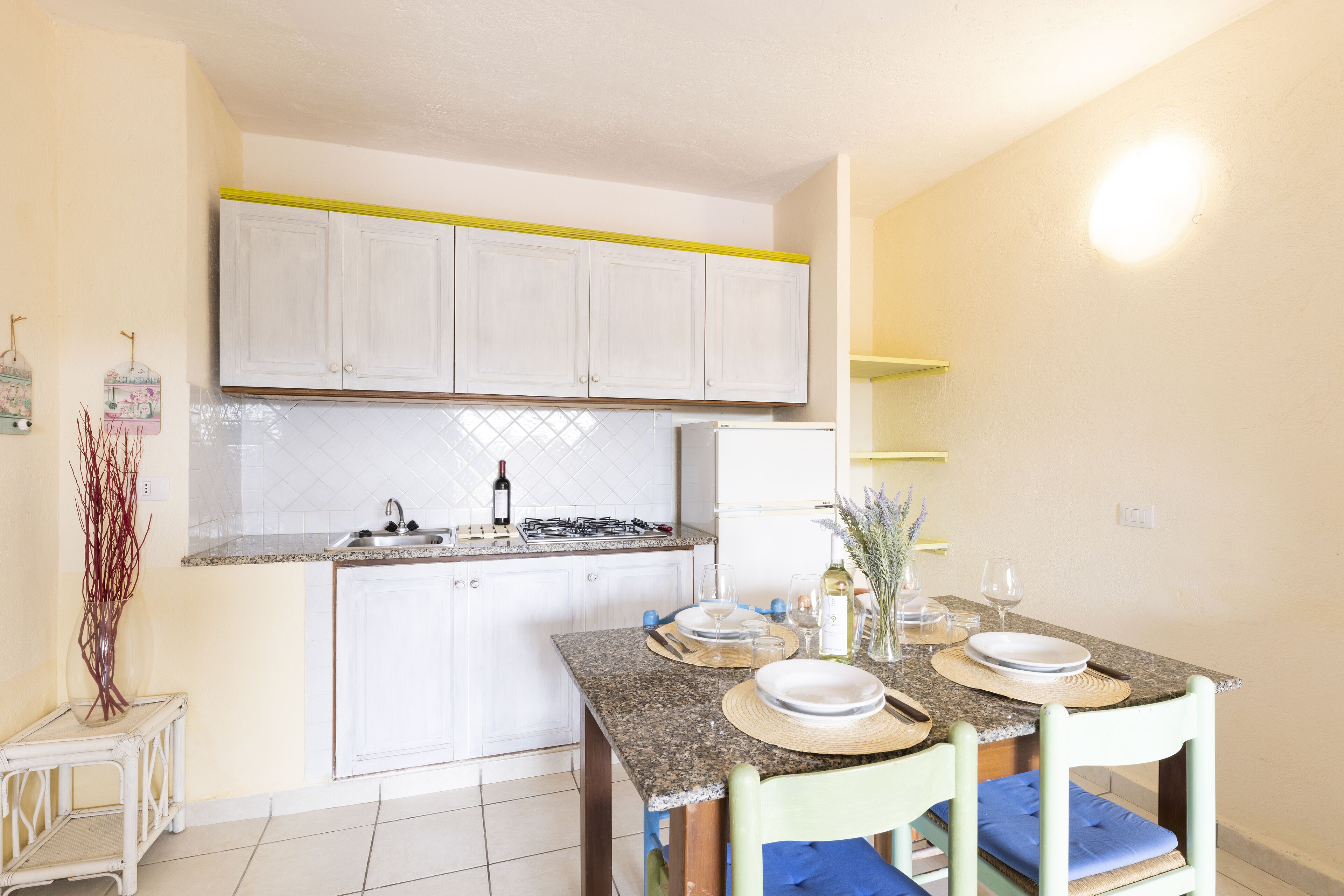 A kitchen with white cabinets, a granite countertop, and a dining area with two chairs and a table set for two.