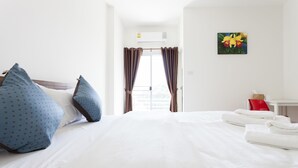 A hotel room with a large bed, white bedding, blue pillows, a red chair, and a painting on the wall. - The Passion (Chiang Mai)