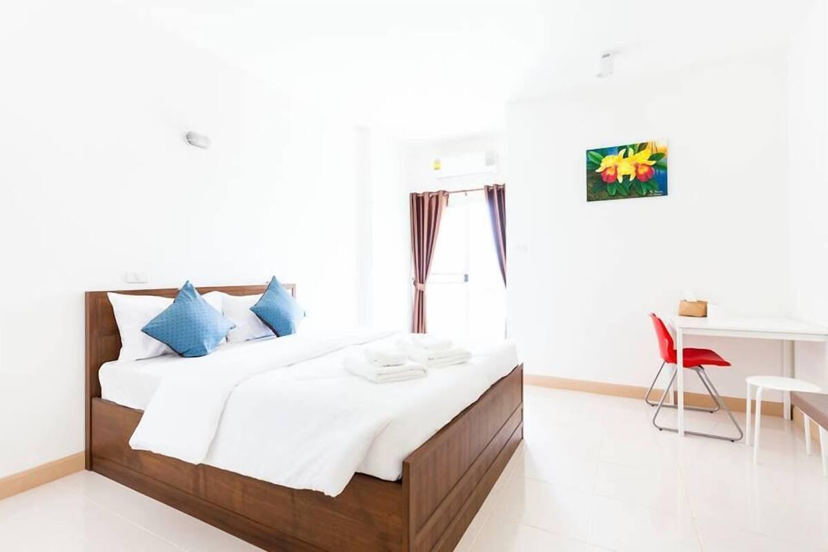 A hotel room with a wooden bed, white bedding, a desk with a chair, and a painting on the wall.