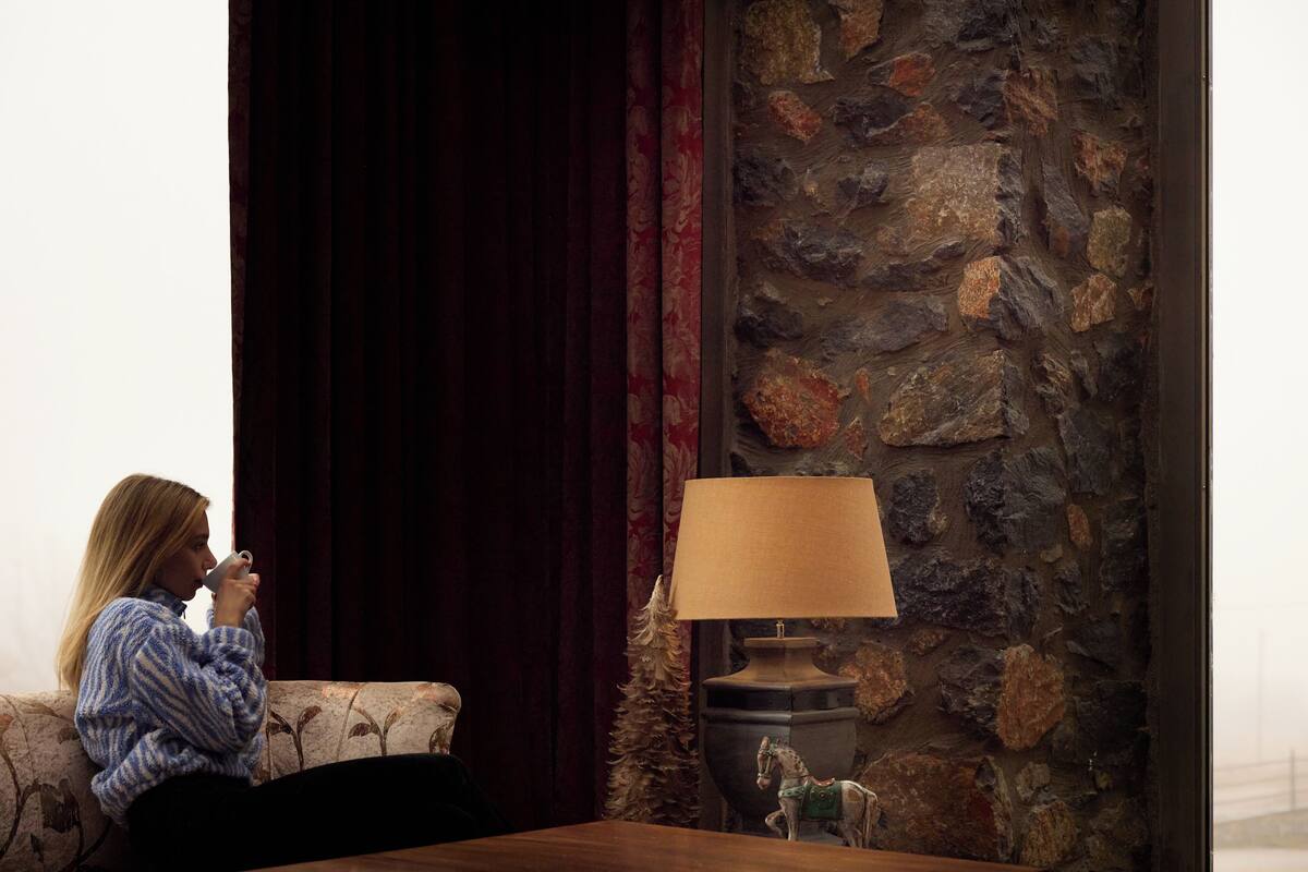 A person sitting on a sofa in a room with a stone wall and a lamp on a table.