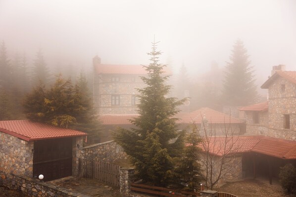 A stone building with a red-tiled roof, surrounded by trees and fog.