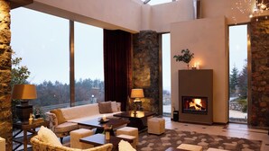 Ein geräumiges Wohnzimmer mit Kamin, großen Fenstern, Steinwänden und bequemen Sitzmöglichkeiten.