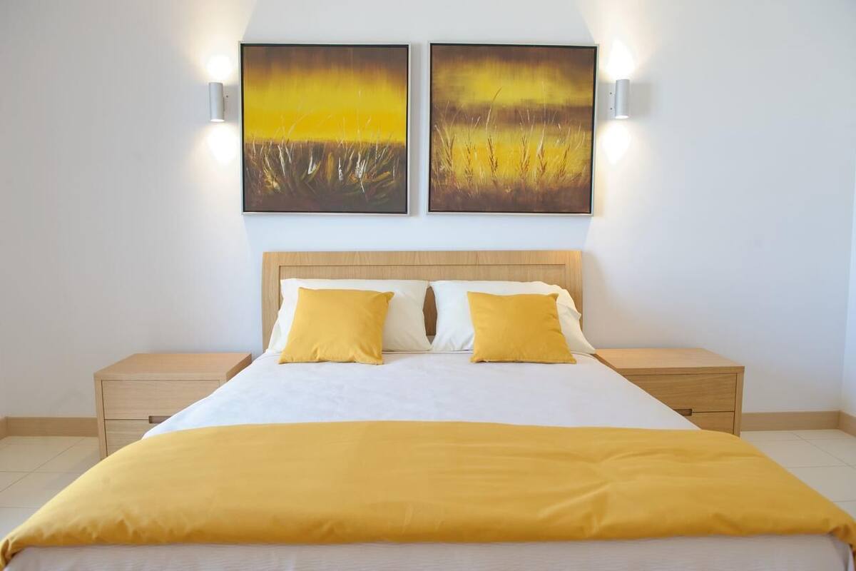 Une chambre d’hôtel avec un grand lit, deux tables de chevet et deux lampes fixées au mur.