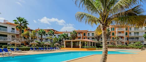 Relax by the clear pool surrounded by lounge chairs and umbrellas, with a covered seating area nearby.