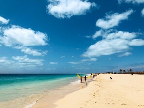 A beach with clear turquoise water, a sandy shore, and a few people and boats. - Agua Hotels Sal Vila Verde Resort (Sal)