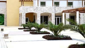 A courtyard with a brick building, green shutters, and palm trees.