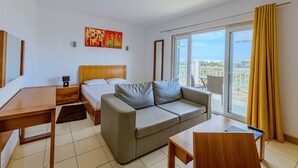 A modern hotel room with a bed, sofa, desk, and balcony with yellow curtains.