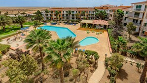 A hotel with multiple swimming pools, palm trees, and a beach view.