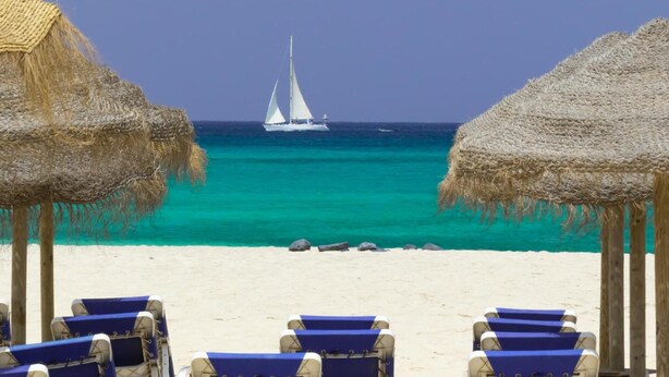 A beach with thatched umbrellas and lounge chairs facing a turquoise sea.