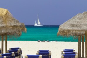 A beach with thatched umbrellas and lounge chairs facing a turquoise sea.