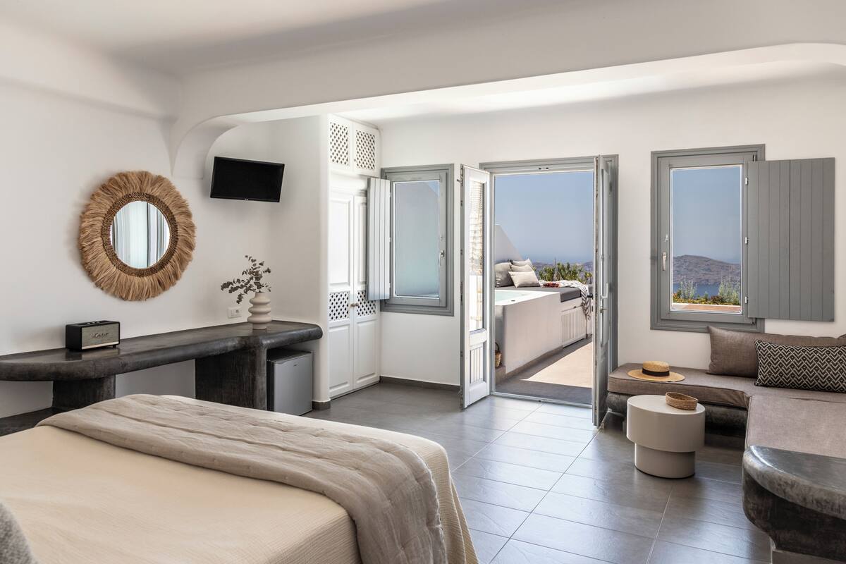 A modern bedroom with a bed, a desk, a TV, and a balcony with a view.