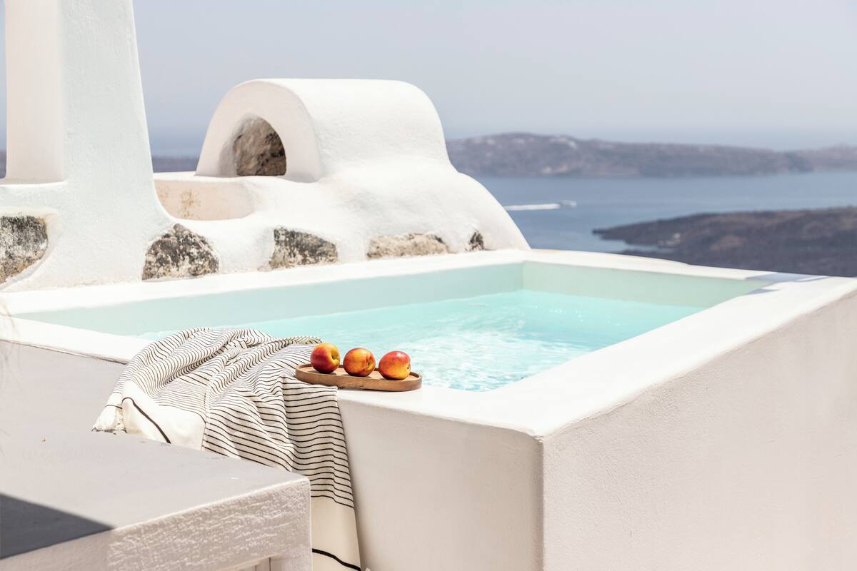 A sunlit outdoor hot tub with a view of the sea and distant islands.