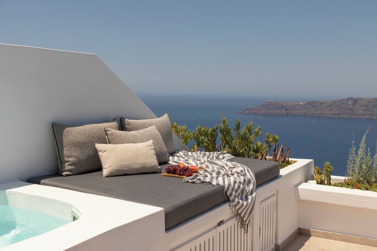 A sunlit outdoor seating area with a view of the sea, a hot tub, and a variety of plants.