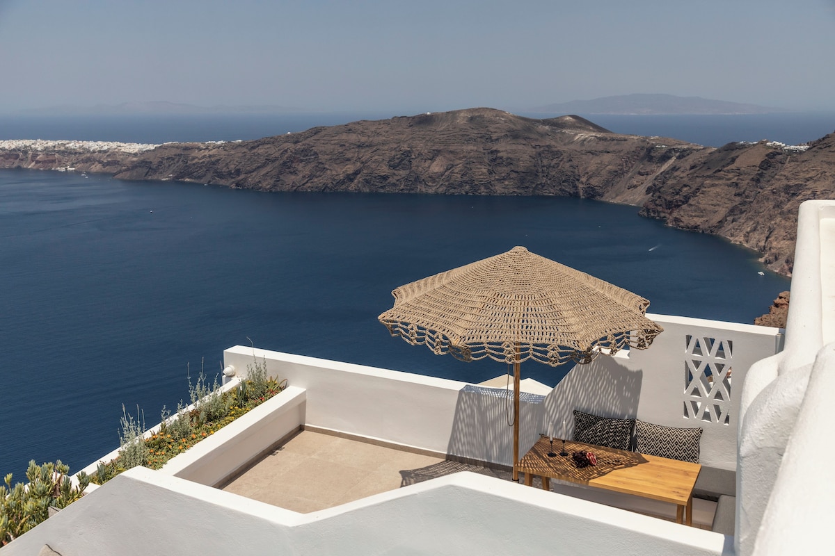 A terrace with a woven umbrella, a wooden table, and a white wall with a lattice design.