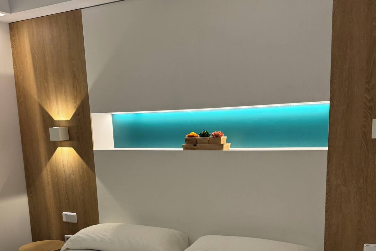 Una habitación de hotel moderna con dos camas, una pared de acento de madera y otra pared de acento en color aguamarina, además de un pequeño estante con objetos decorativos.