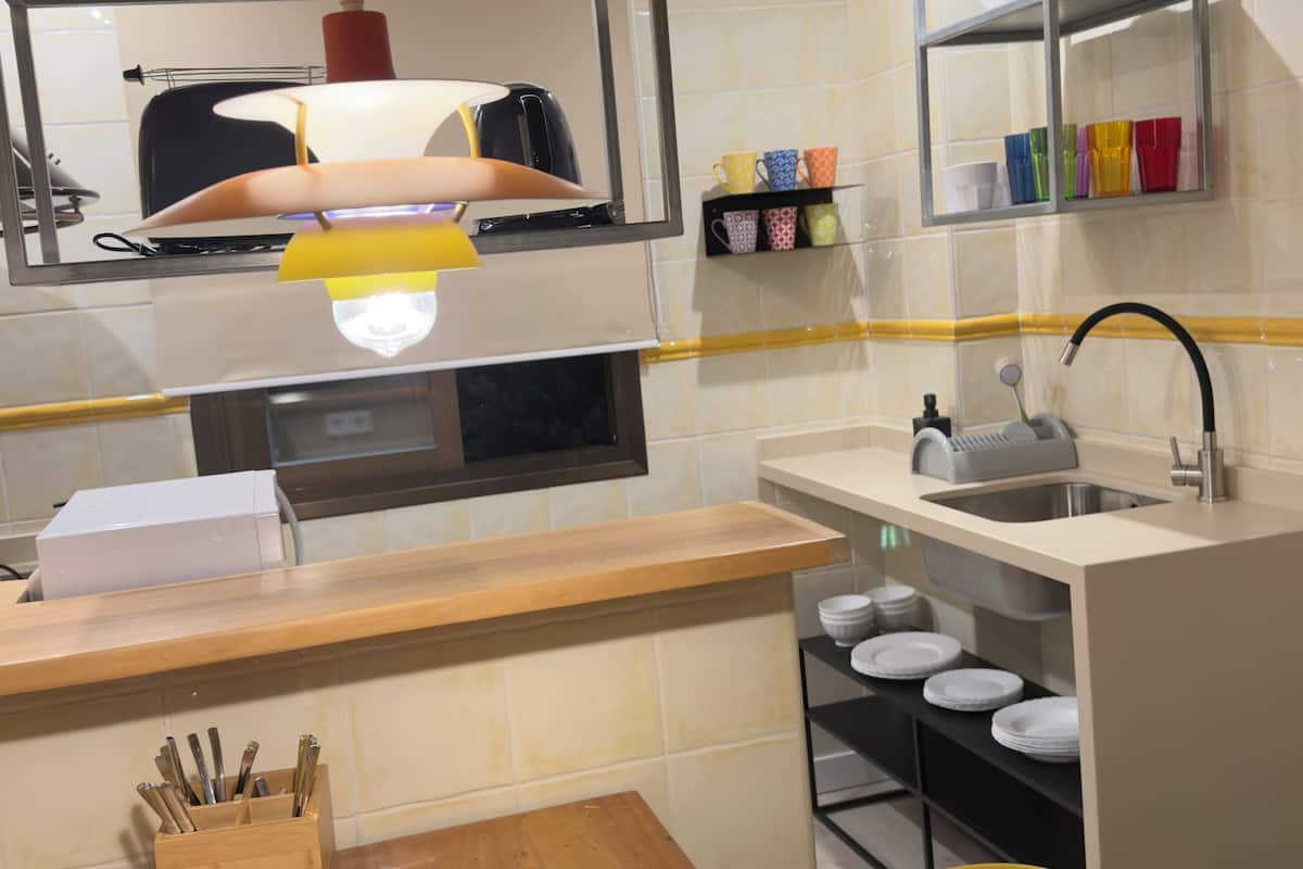 Una cocina con mostrador de madera, una silla amarilla, un lavabo y una estantería con tazas de colores.