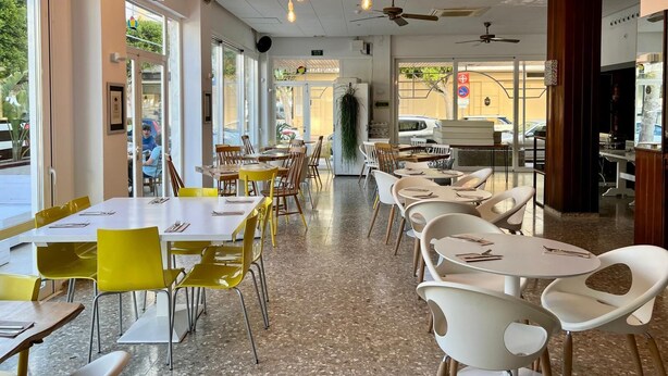 Interior de restaurante con varias mesas y sillas, ventiladores de techo y lámparas colgantes.