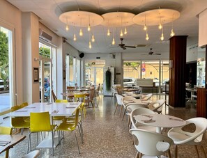 Interior de restaurante con varias mesas y sillas, ventiladores de techo y lámparas colgantes.