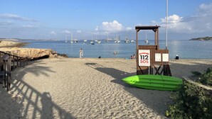Una playa con una torre de salvavidas, un kayak verde y veleros al fondo.