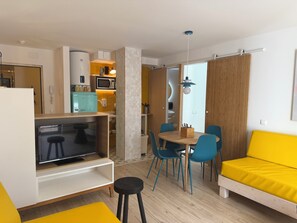 Un espacio habitable compacto con kitchenette, comedor con sillas, sofá y televisor.