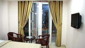 Une chambre d’hôtel avec un lit, deux chaises, une petite table, un téléviseur et de grandes fenêtres avec des rideaux.