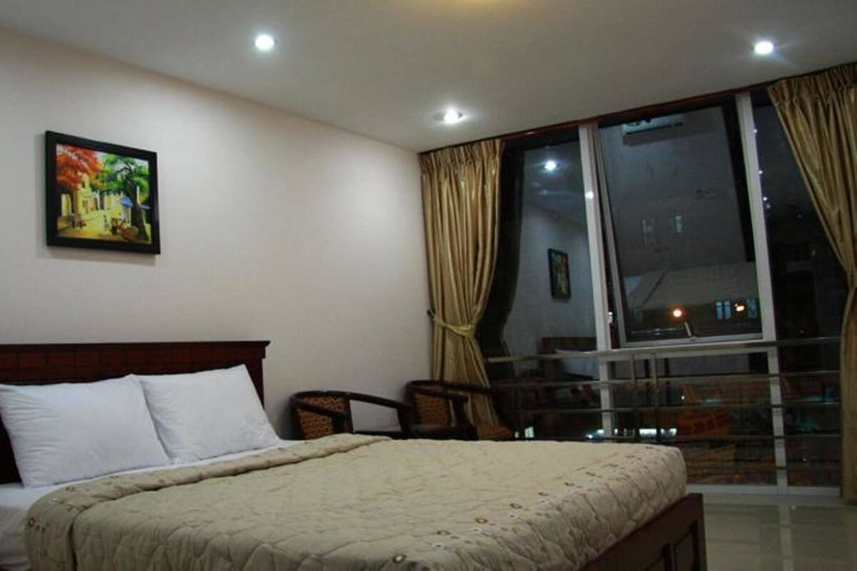 Ein Hotelzimmer mit einem Bett, einem Sessel, einem Fenster mit Vorhängen und einem Bild an der Wand.