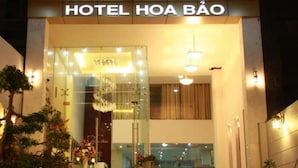 L'entrée de l'HÔTEL HOA BÃO présente un design moderne, avec une façade en verre, des plantes d'intérieur et un lustre accueillant.