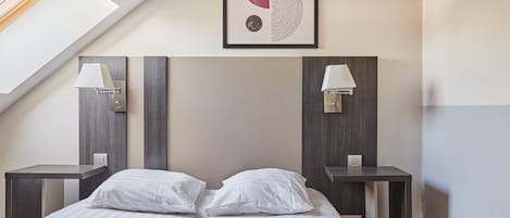A modern hotel room with a large bed, two bedside tables with lamps, a ceiling skylight, and a wall-mounted abstract art piece.