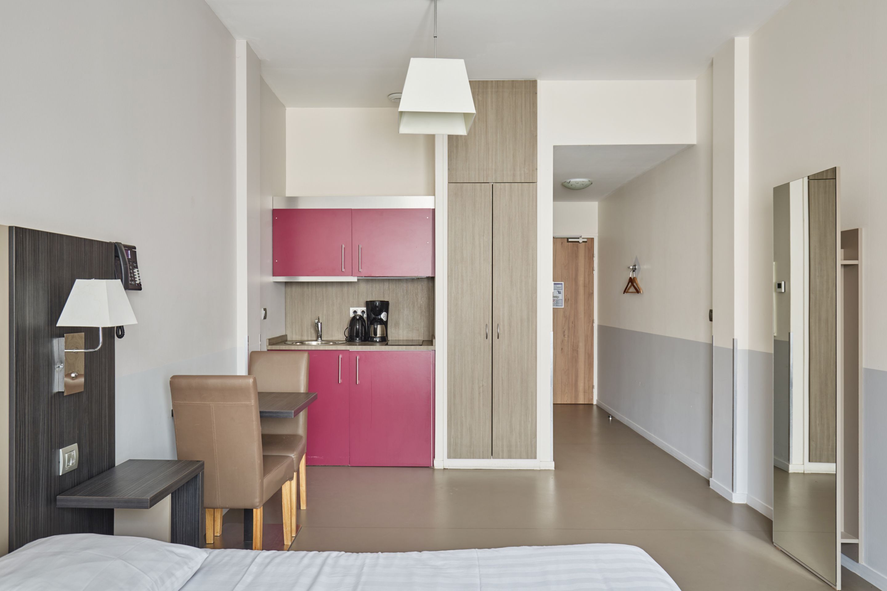 Une chambre d’hôtel moderne équipée d’un lit, d’un bureau, d’une chaise, d’une kitchenette et d’une salle de bain.