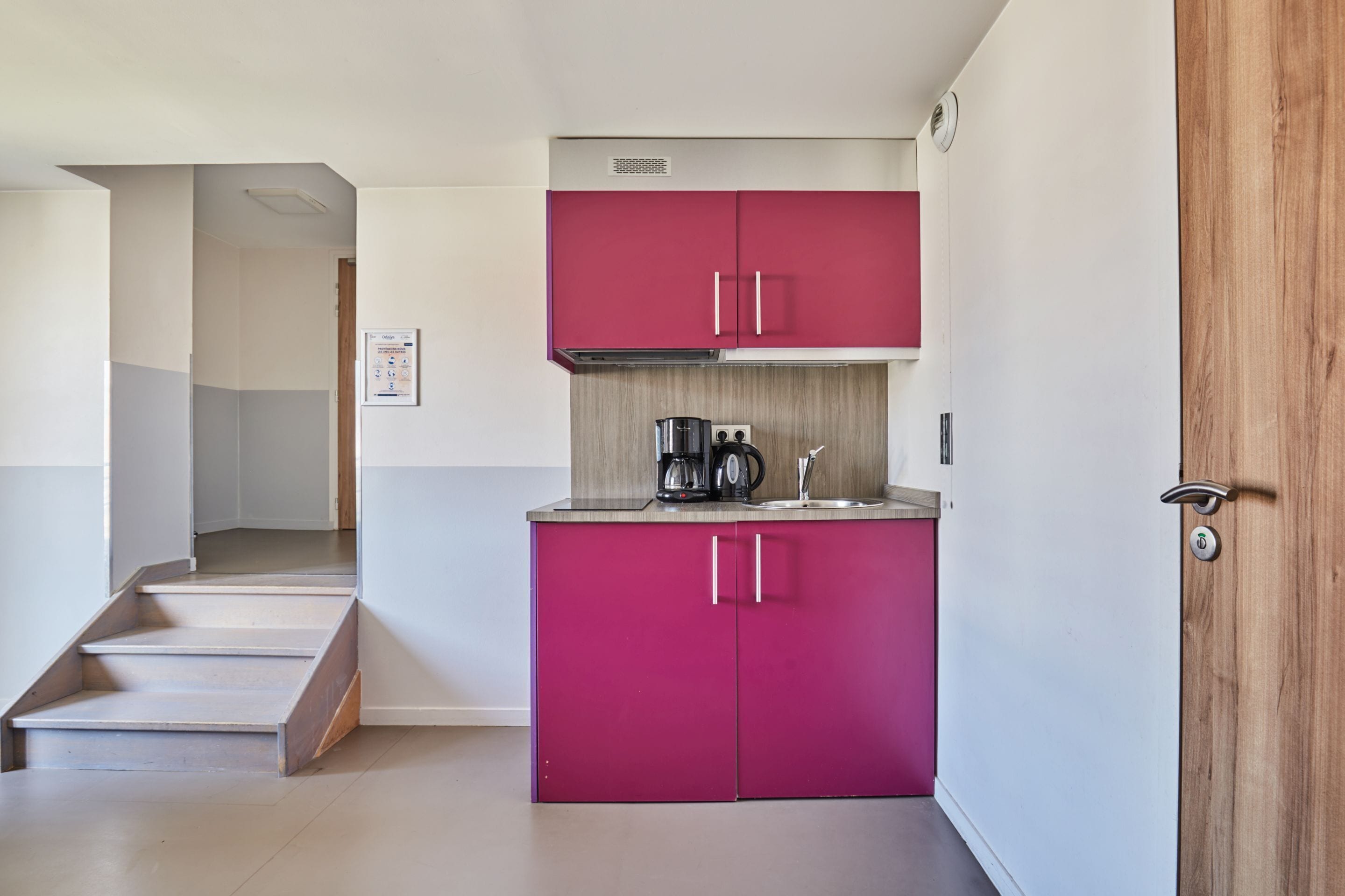 A modern kitchen with pink cabinets, a coffee maker, and a sink.
