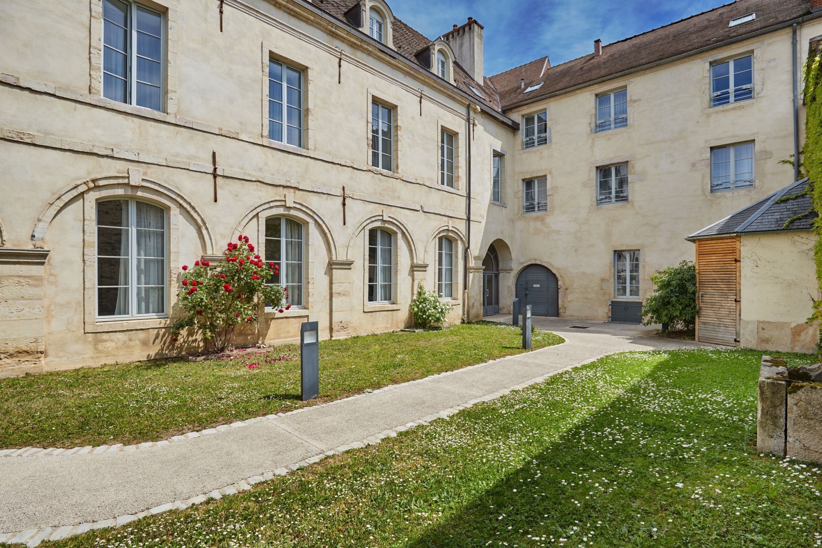A courtyard with a paved walkway, stone walls, and a small garden with flowers.