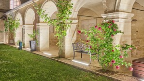 An indoor courtyard with stone arches, a bench, and flowering plants. - Appart'hôtel Odalys City - Dijon Centre Les Cordeliers (Dijon)