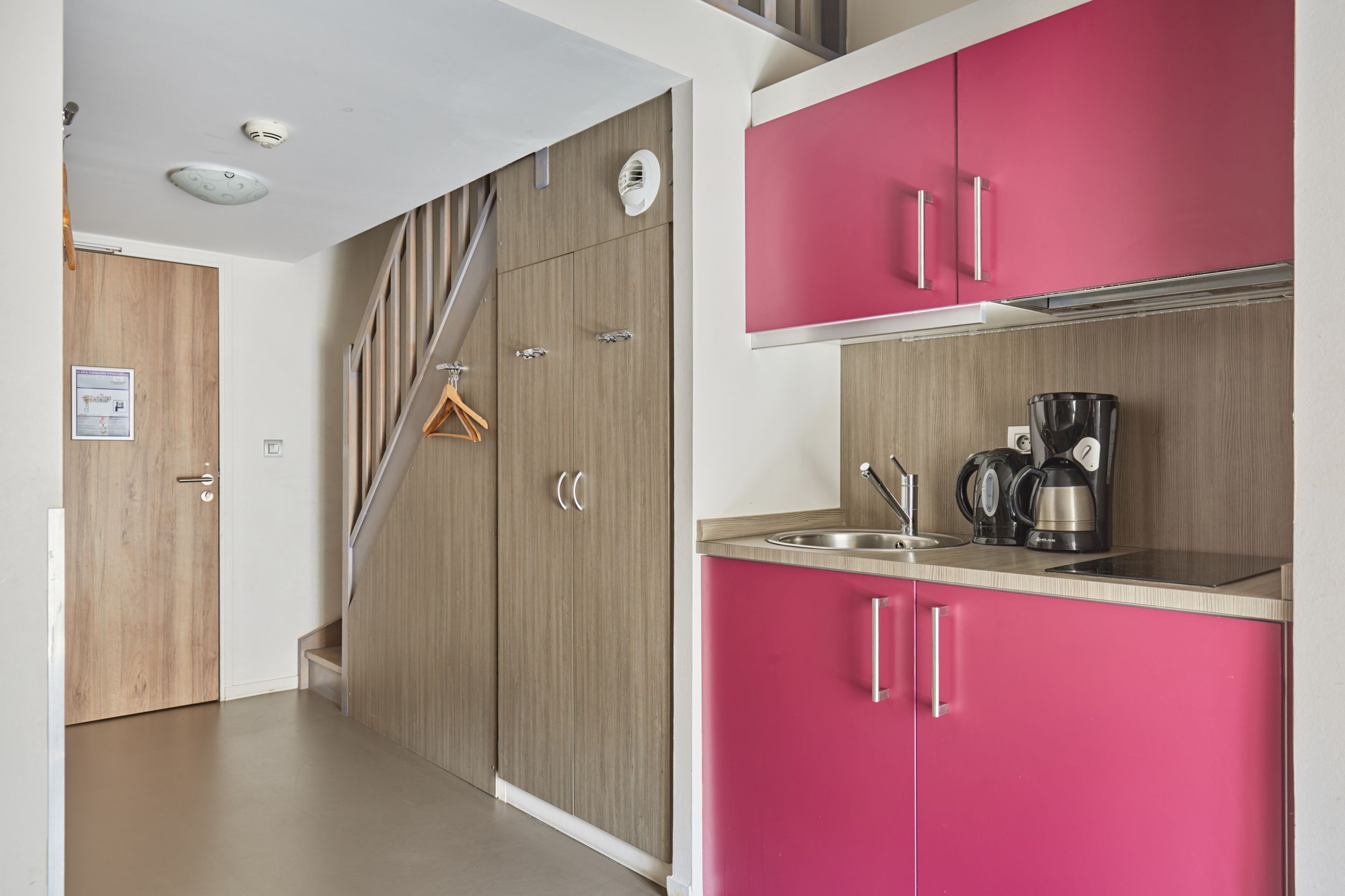 A kitchen with pink cabinets, a stainless steel sink, and a coffee maker.