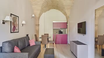 Uma sala de estar moderna com um sofá cinzento, almofadas cor-de-rosa, uma mesa de centro e uma TV na parede.