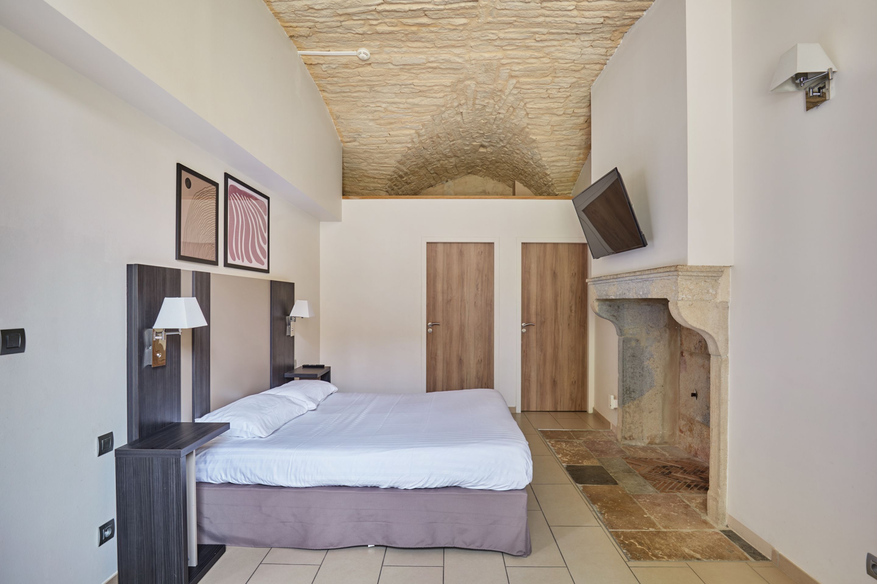 Un dormitorio con techo de piedra, una cama, un televisor montado en la pared y una chimenea.