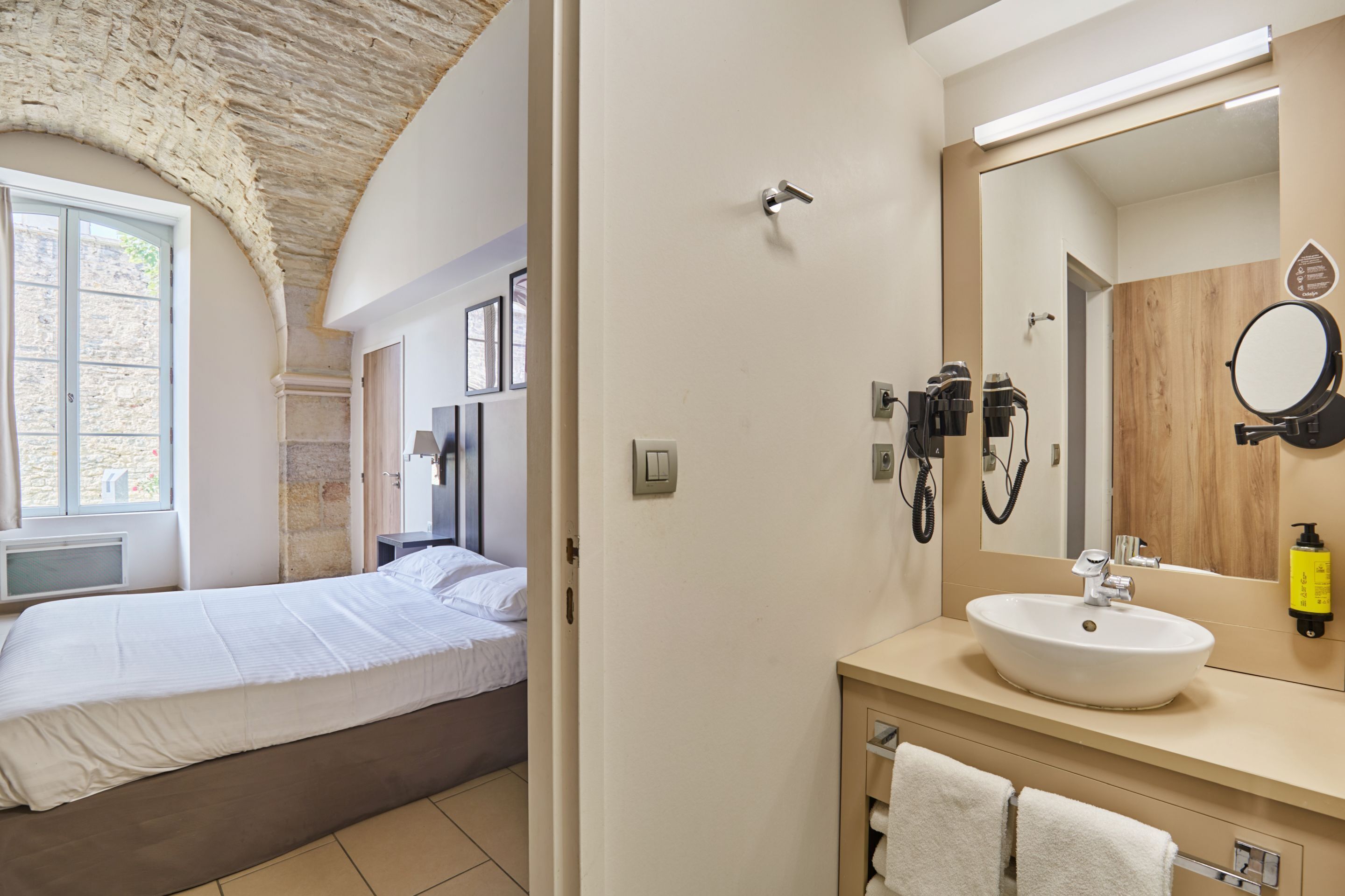 Une chambre avec un lit, une salle de bain avec un lavabo et un miroir, et un plafond en pierre.